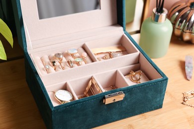 Photo of Elegant jewelry box with beautiful bijouterie and expensive wristwatch on wooden table, closeup