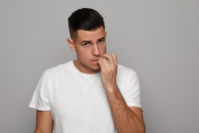 Photo of Man biting his nails on grey background. Bad habit