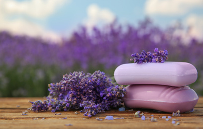 Photo of Fresh lavender flowers and soap bars on wooden table outdoors, closeup