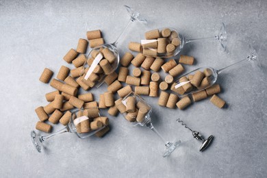 Glasses with many wine corks and corkscrew on light grey table, flat lay