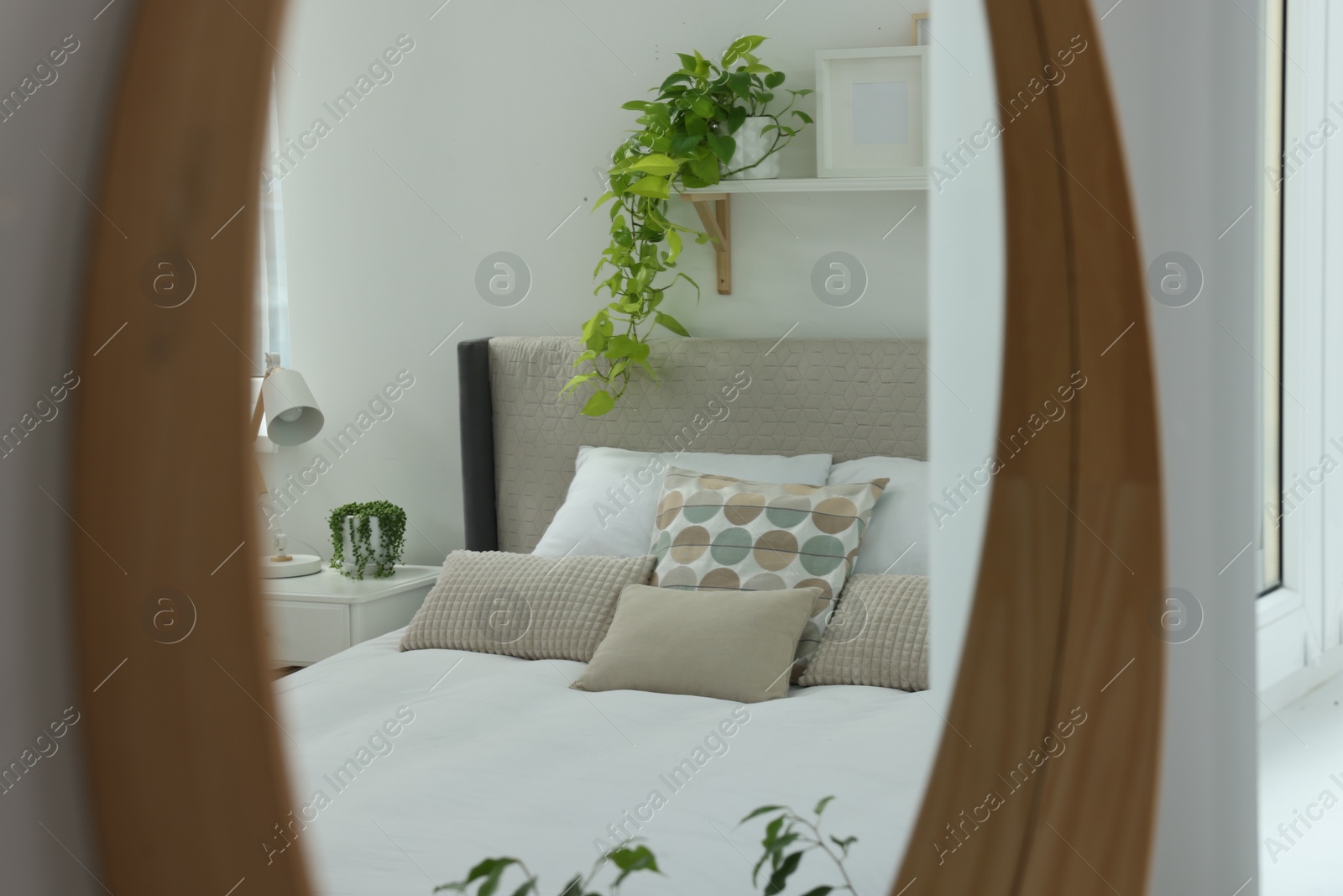 Photo of Reflection of large comfortable bed and bedside table in mirror on white wall