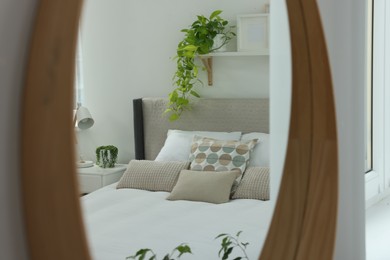 Photo of Reflectionlarge comfortable bed and bedside table in mirror on white wall