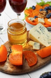 Photo of Delicious persimmon, blue cheese and honey on white wooden table, closeup