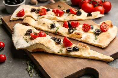 Photo of Focaccia bread with olives and tomatoes on grey table, closeup