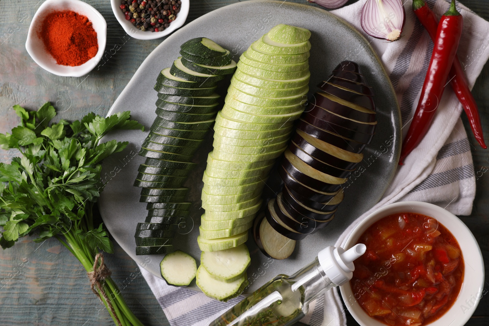 Photo of Fresh ripe vegetables, parsley and dressing for ratatouille on light blue wooden table, flat lay