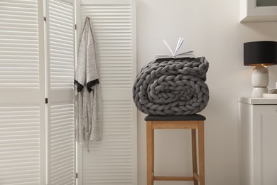 Photo of Wooden stool with rolled chunky knit blanket and book in room