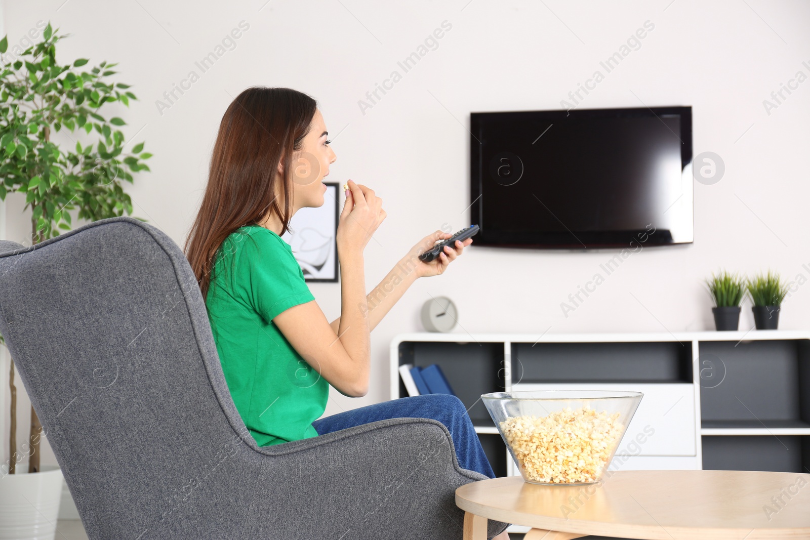 Photo of Young woman watching TV in armchair at home