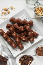 Photo of Tasty chocolate bars with nuts on white wooden table, flat lay