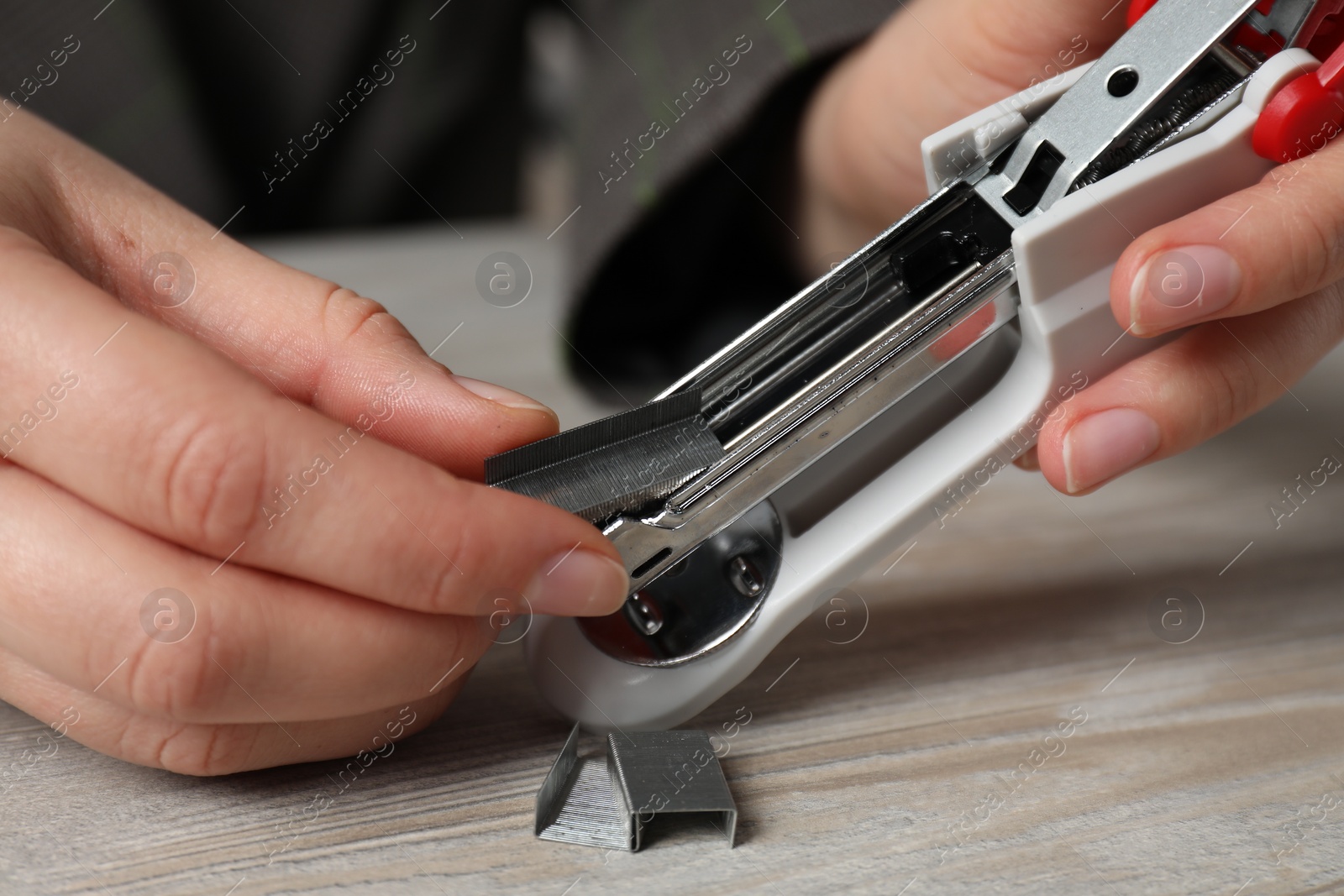 Photo of Woman putting metal staples into stapler at wooden table, closeup