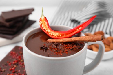 Cup of hot chocolate with chili pepper and cinnamon on white marble table, closeup