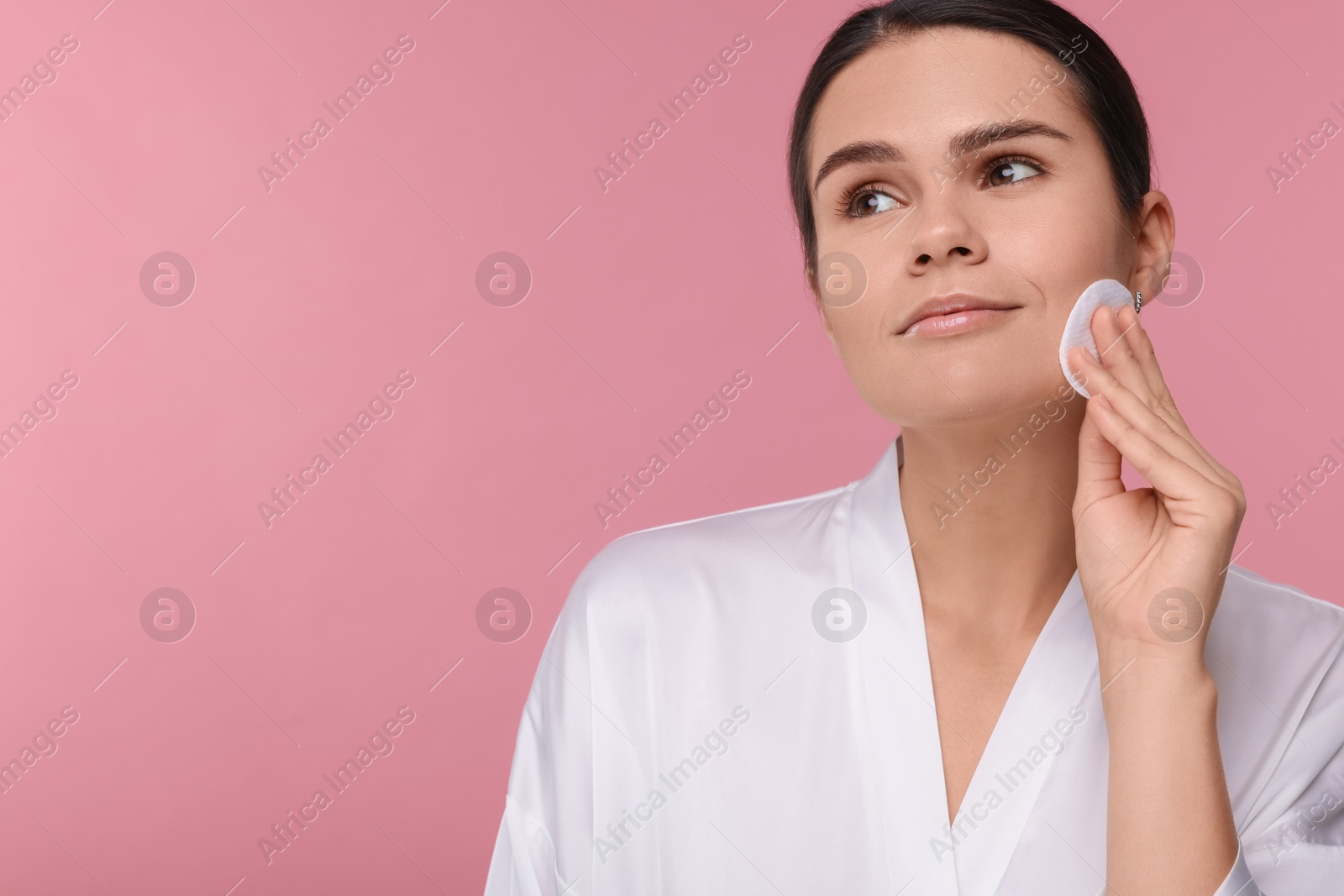 Photo of Young woman cleaning her face with cotton pad on pink background. Space for text