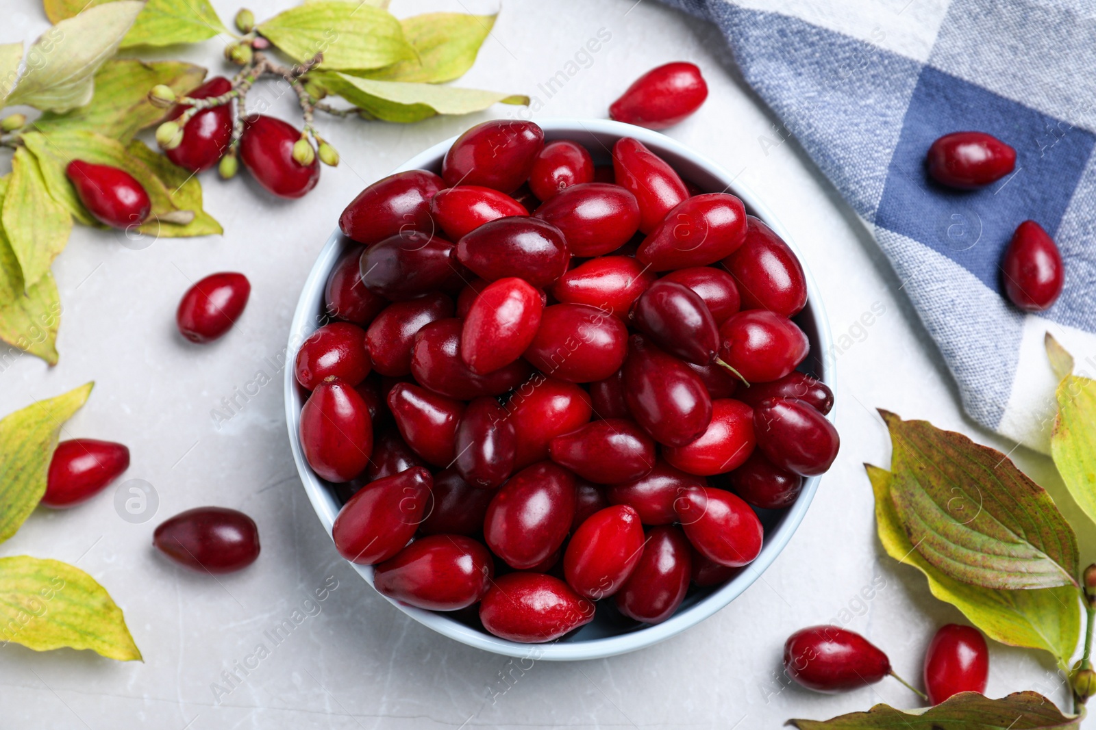 Photo of Fresh ripe dogwood berries, leaves and napkin on light grey table, flat lay