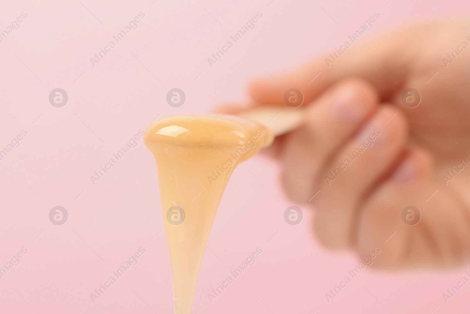 Photo of Woman holding spatula with hot depilatory wax on light background, closeup