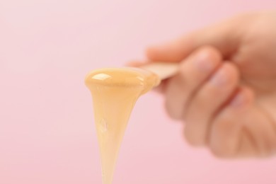 Woman holding spatula with hot depilatory wax on light background, closeup