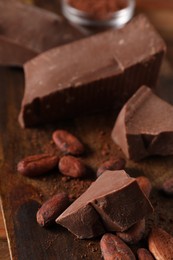Photo of Pieces of tasty milk chocolate, powder and cocoa beans on wooden table, closeup