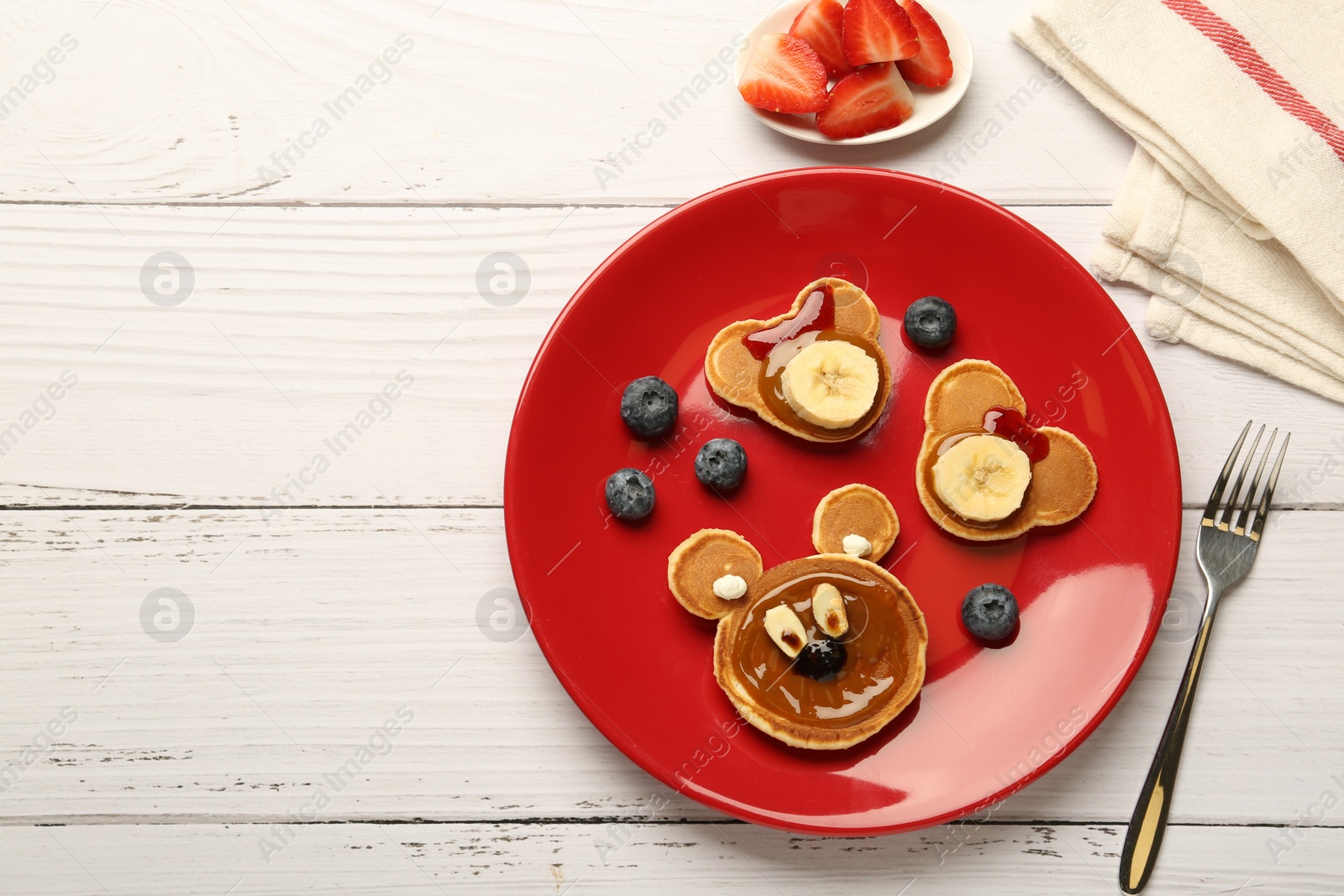 Photo of Creative serving for kids. Plate with cute bears made of pancakes, berries, banana and chocolate paste on white wooden table, flat lay. Space for text