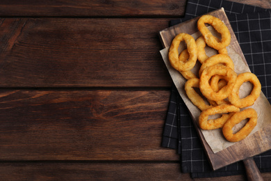 Photo of Fried onion rings served on wooden table, top view. Space for text