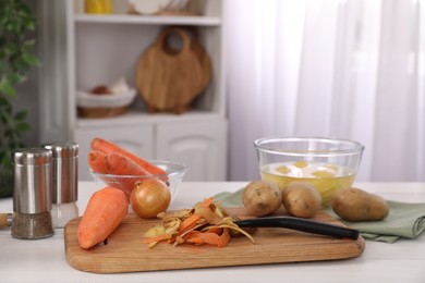 Peels of fresh vegetables and peeler on white wooden table indoors