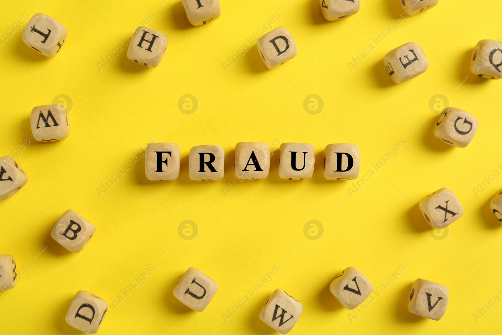 Photo of Word Fraud of wooden cubes with letters on yellow background, flat lay