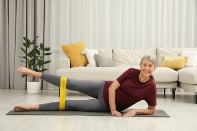 Photo of Senior woman doing exercise with fitness elastic band on mat at home