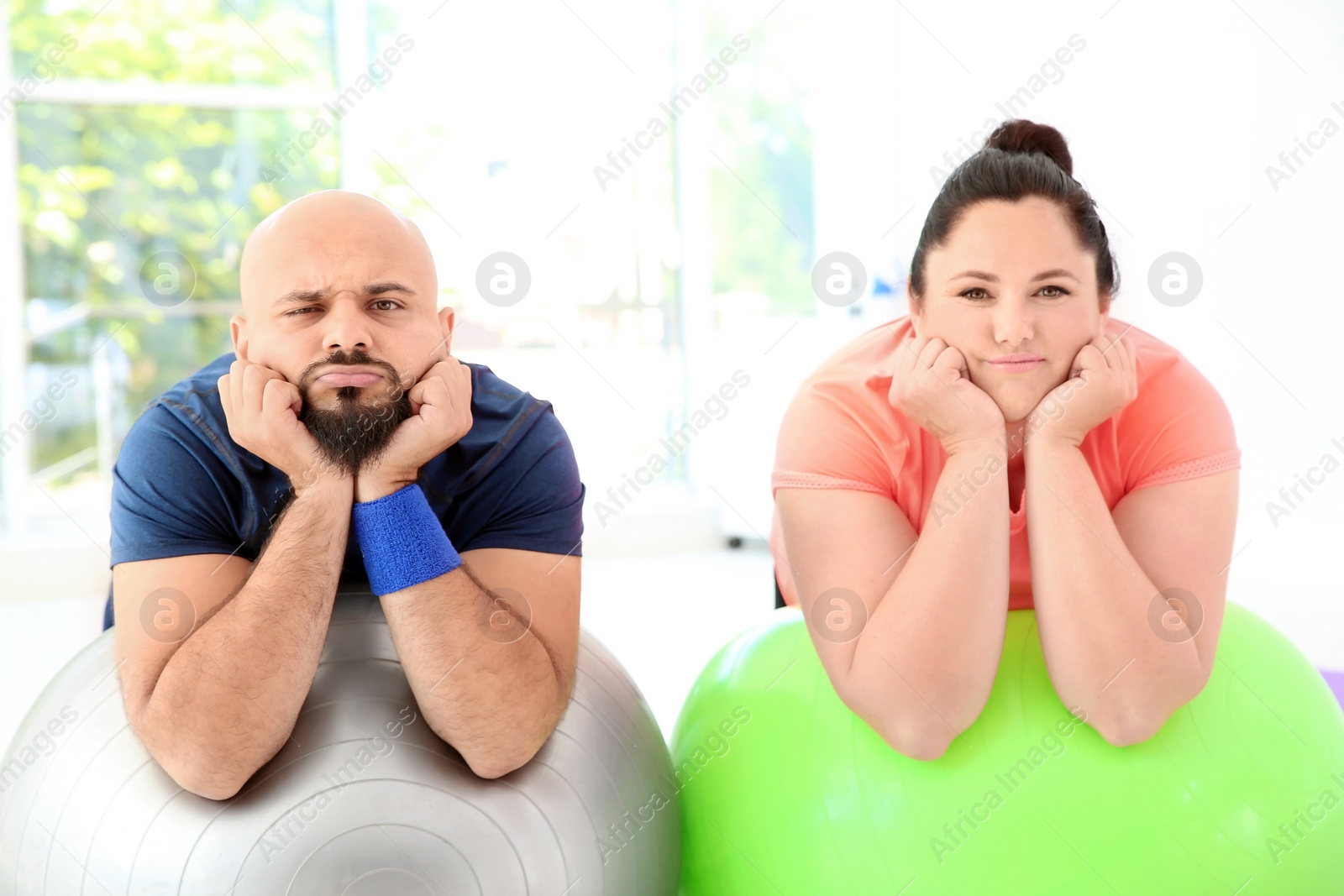 Photo of Tired overweight man and woman resting on fitness balls in gym