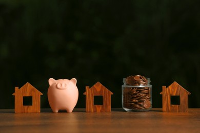 Piggy bank, jar of coins and house models on wooden table