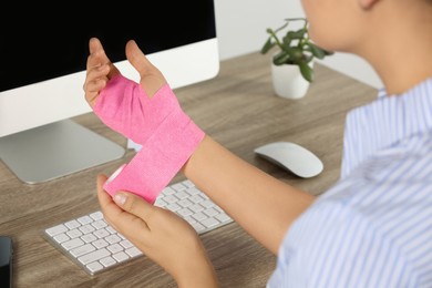 Photo of Young woman applying medical bandage onto hand at workplace, closeup