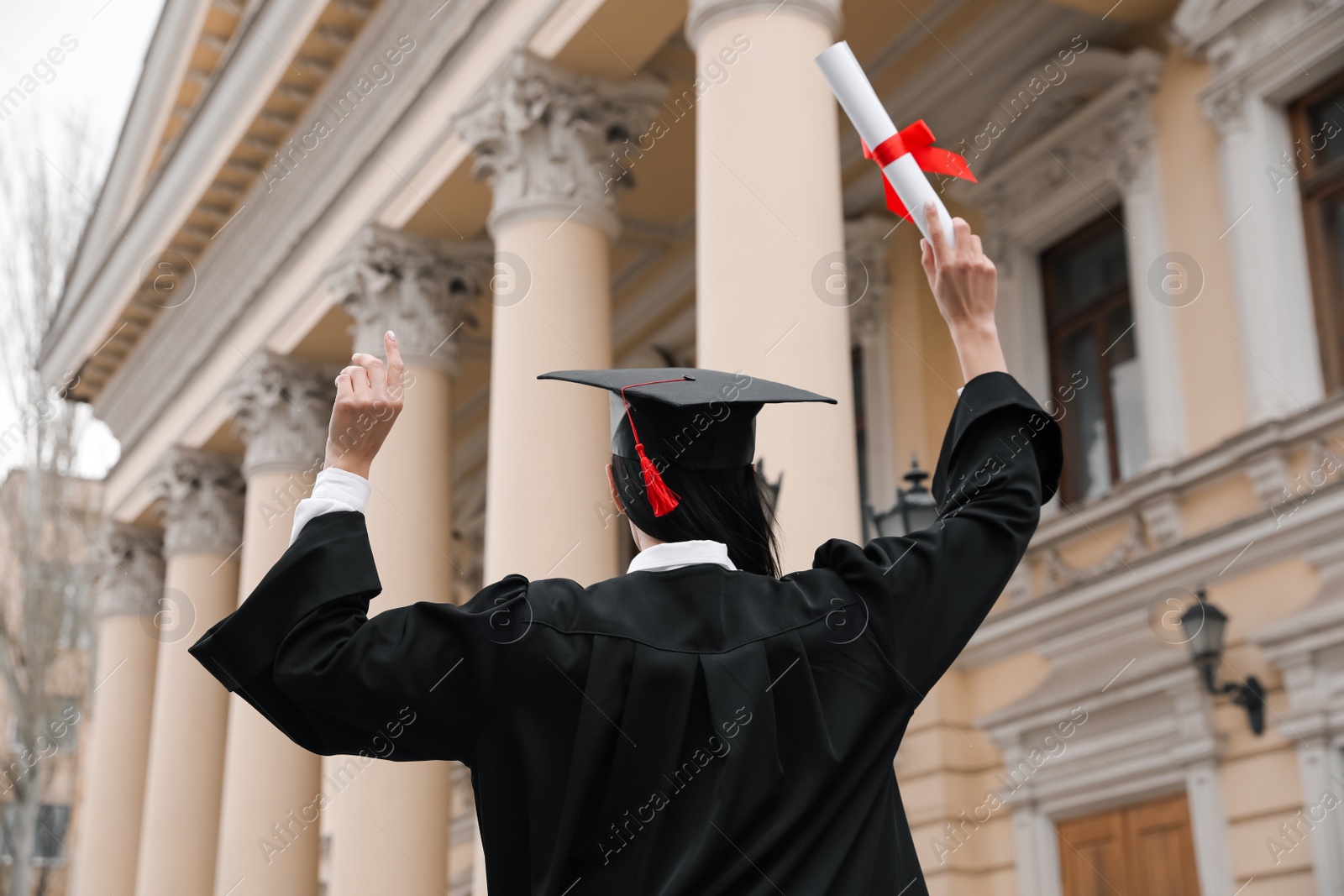 Photo of Student with diploma after graduation ceremony outdoors, back view