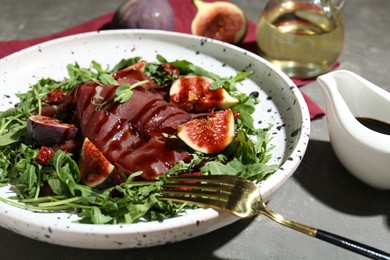 Photo of Plate of tasty bresaola salad with figs, sun-dried tomatoes, balsamic vinegar and fork on grey table, closeup