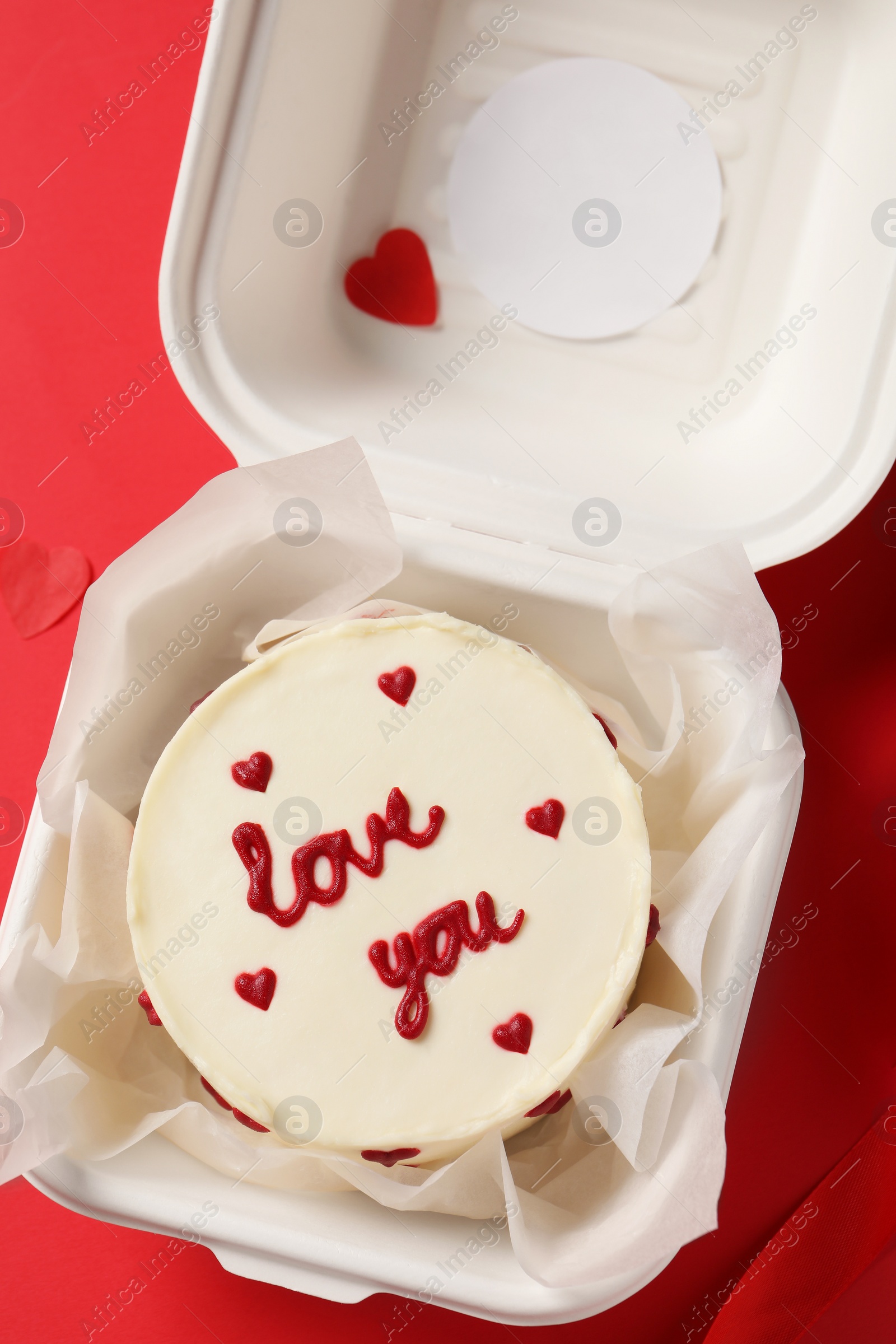 Photo of Bento cake with Love You text in takeaway box on red table, top view. St. Valentine's day surprise