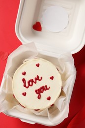 Bento cake with Love You text in takeaway box on red table, top view. St. Valentine's day surprise