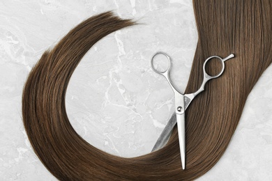 Flat lay composition with brown hair and scissors on grey background. Hairdresser service
