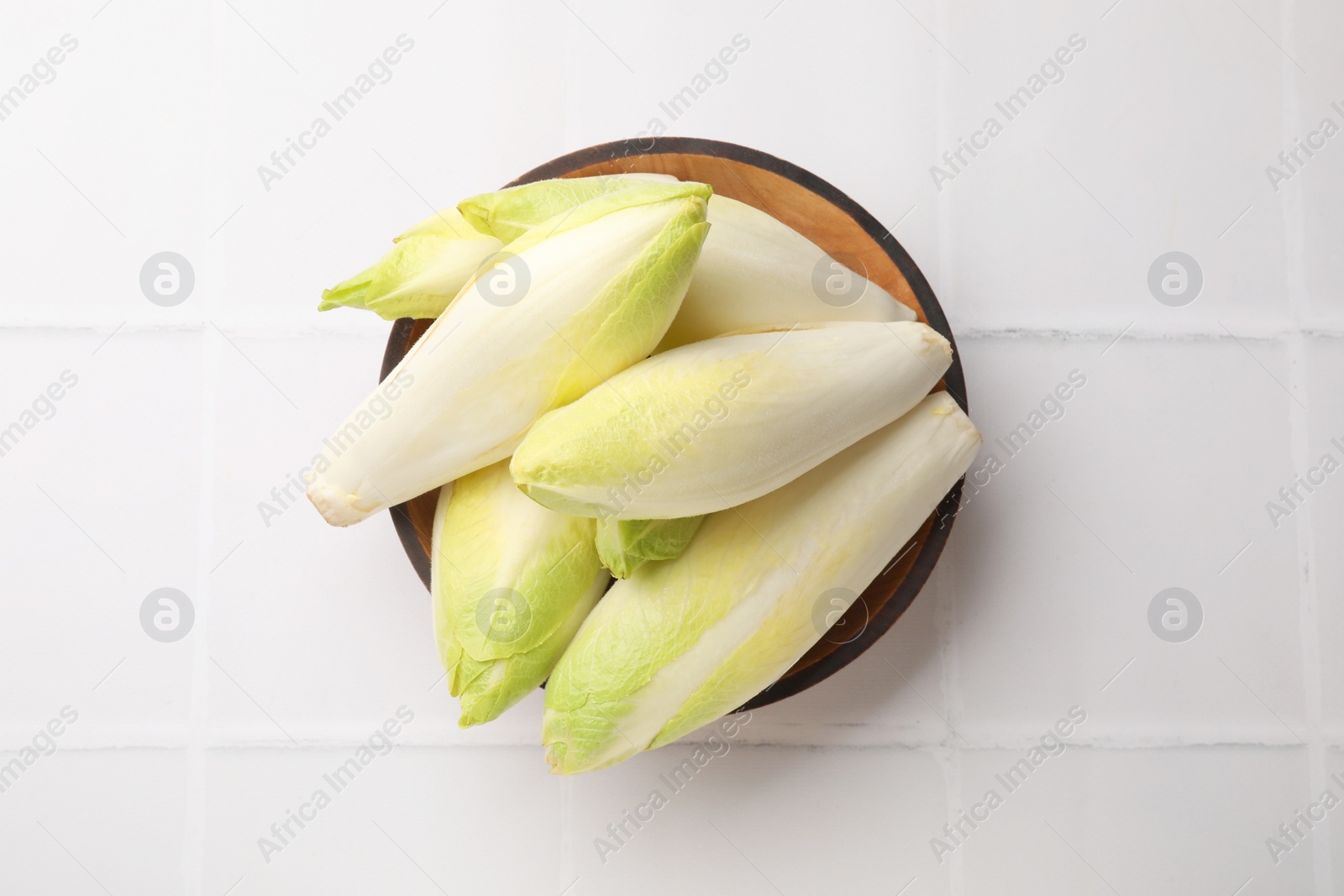 Photo of Fresh raw Belgian endives (chicory) in bowl on white tiled table, top view