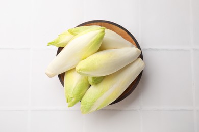 Photo of Fresh raw Belgian endives (chicory) in bowl on white tiled table, top view
