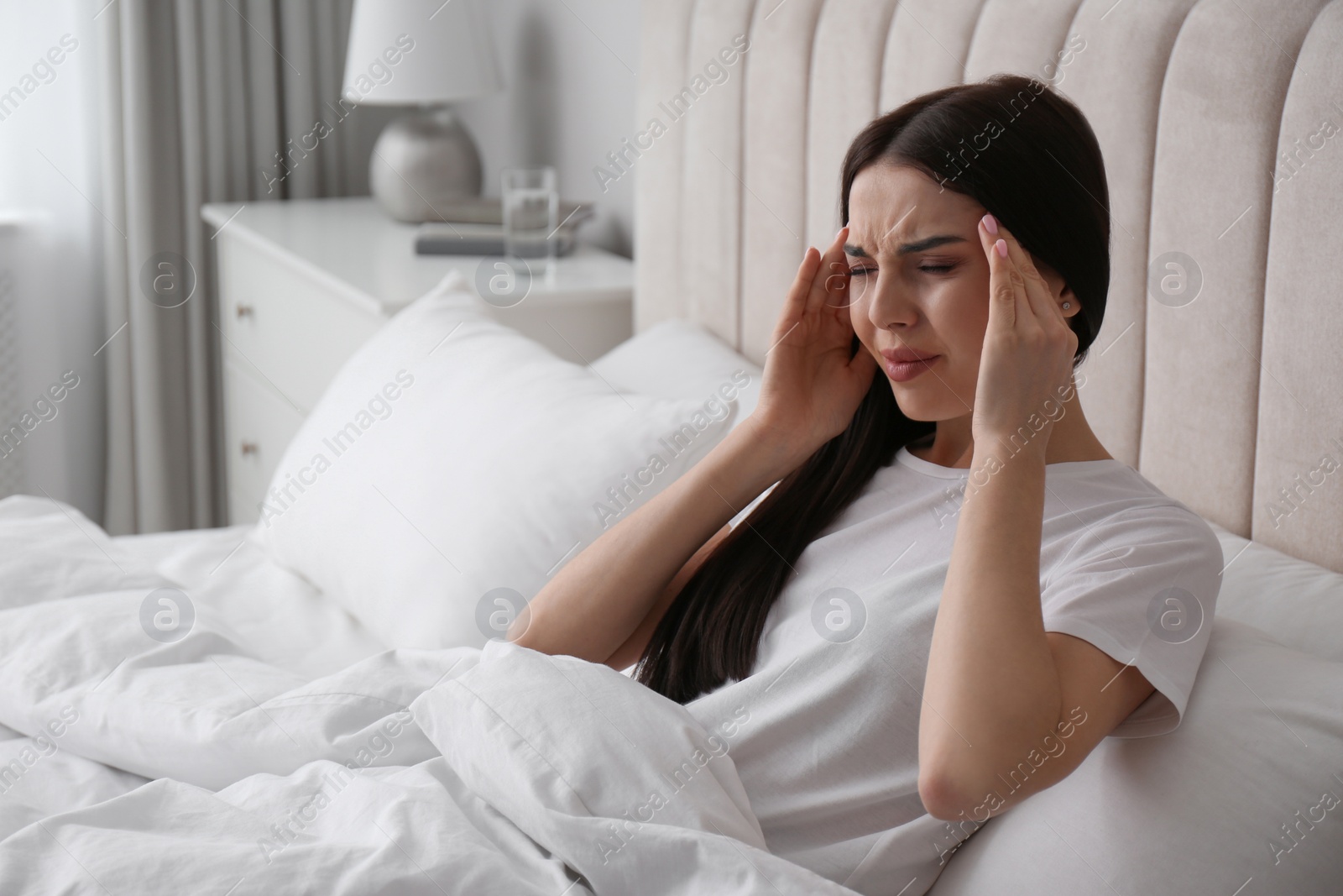 Photo of Young woman suffering from migraine in bed at home, space for text