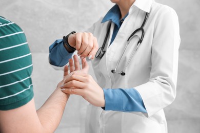 Doctor checking patient's pulse during consultation near grey wall, closeup