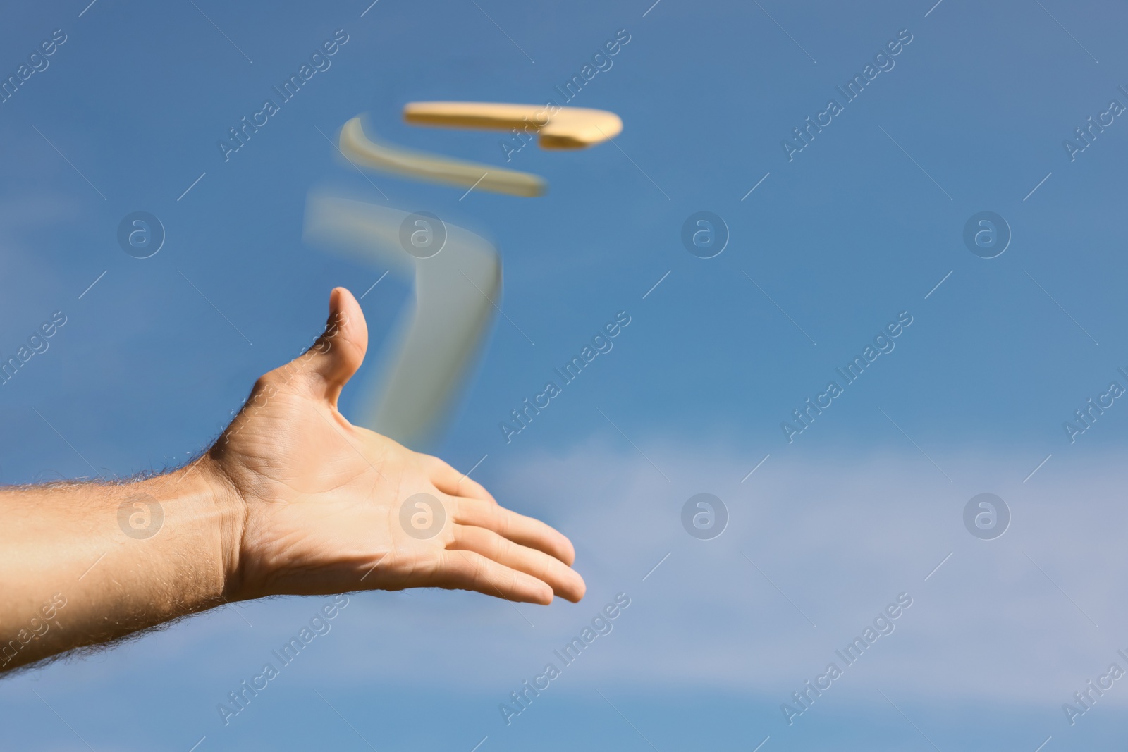 Image of Man throwing boomerang against blue sky, closeup