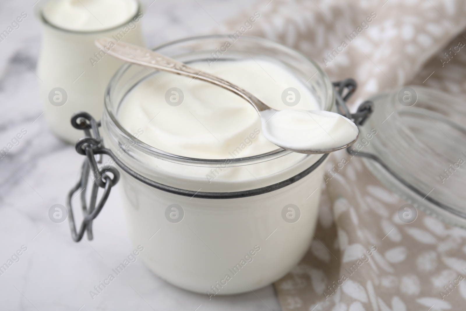 Photo of Delicious natural yogurt in glass jar and spoon on white marble table, closeup