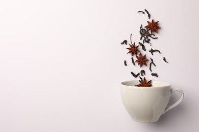 Photo of Anise stars and dry tea falling into cup on white background, flat lay. Space for text