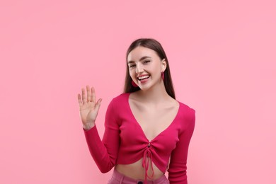 Photo of Beautiful woman in pink clothes waving hello on color background