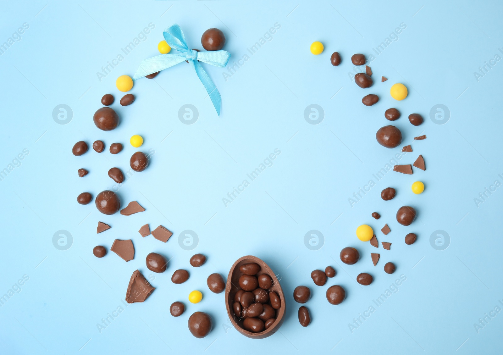 Photo of Frame of delicious chocolate Easter egg and candies on light blue background, flat lay. Space for text