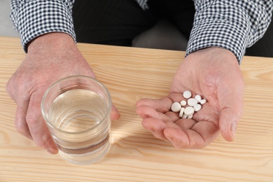 Senior man holding pills and glass of water at table, closeup