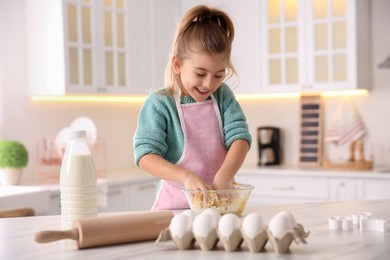 Photo of Little girl making dough at table in kitchen