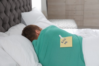 Yellow note with text "Kick me" attached to sleeping man's back. April Fool's day