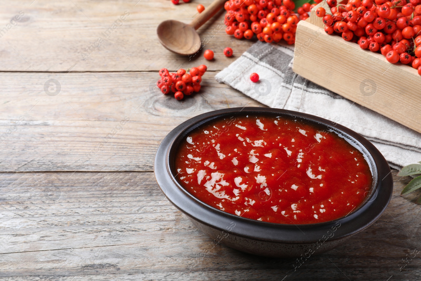 Photo of Delicious rowan jam in bowl on wooden table. Space for text