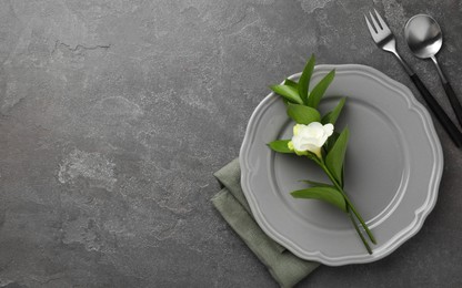 Stylish setting with cutlery, napkin, flower and plate on grey textured table, flat lay. Space for text