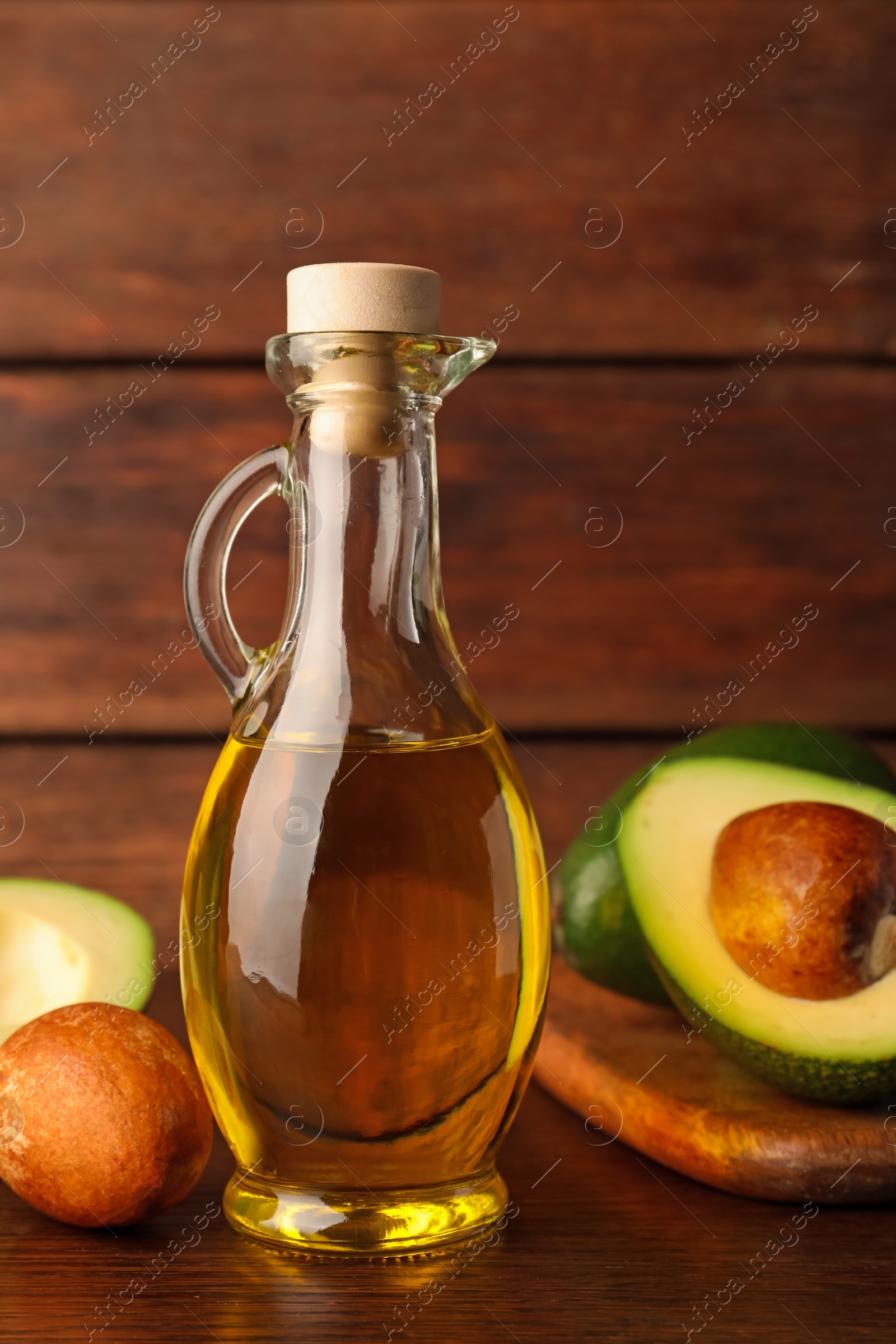 Photo of Glass jug of cooking oil and fresh avocados on wooden table