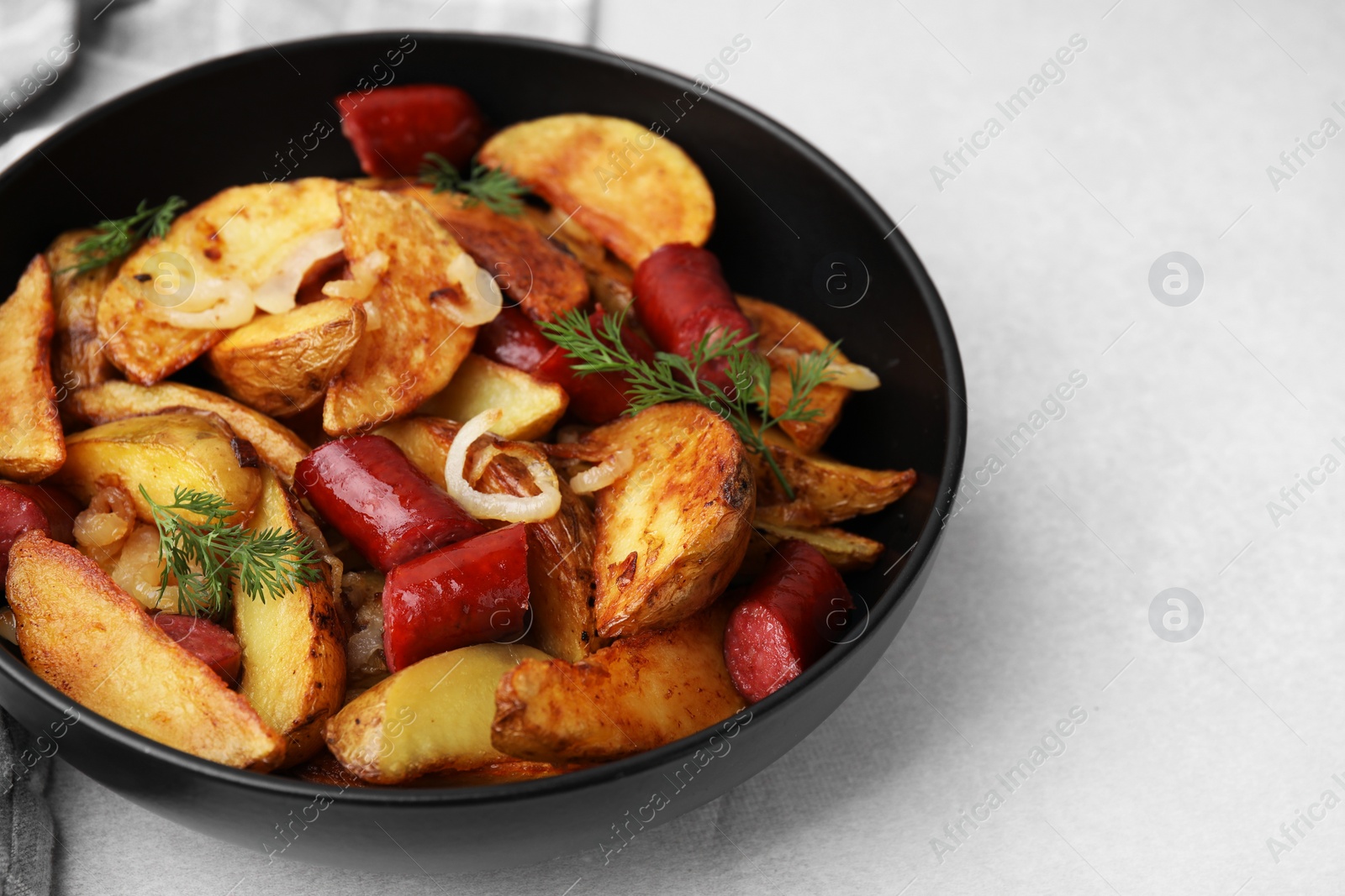 Photo of Delicious baked potato with thin dry smoked sausages, onion and dill in bowl on gray table, closeup