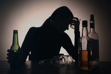 Photo of Alcohol addiction. Silhouette of woman with beer on wooden table, backlit