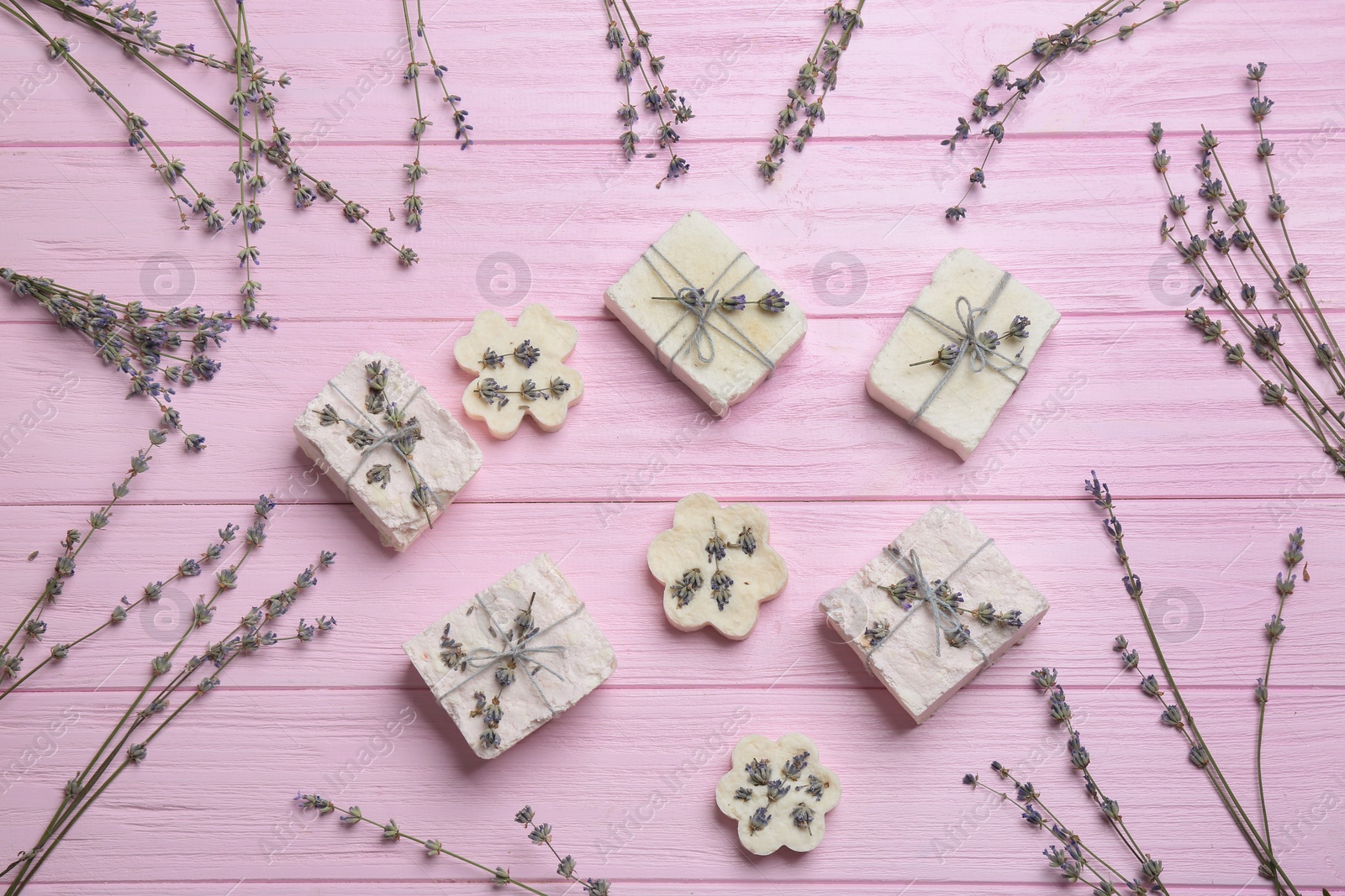 Photo of Hand made soap bars with lavender flowers on pink wooden table, flat lay